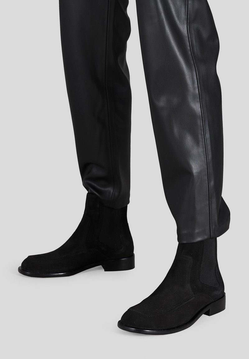 Stivaletti alla caviglia in suede nero con pannelli elastici laterali e un design elegante. La suola è nera lucida, con una silhouette minimalista e moderna.