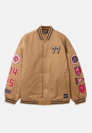 Chaqueta bomber marrón con parches negros y rojos, incluyendo gráficos de '77' y del club universitario. Presenta puños a rayas y cierre de botón a presión.