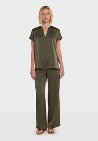 Blusa verde oliva a maniche corte con scollo a V, abbinata a pantaloni a gamba larga dello stesso colore. Tessuto liscio e leggero con una leggera lucentezza.