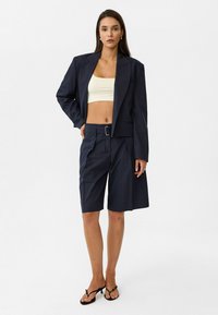 Marineblauw gestreepte blazer en bijpassende shorts van gladde stof; de blazer heeft een enkele knoopsluiting en gestructureerde schouders.