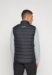 Zwarte gewatteerde vest met hoge kraag, met horizontaal doorgestikt ontwerp en logo. Gekozen over een lichtgrijze lange mouwen shirt.