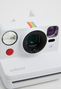 Appareil photo Polaroid blanc avec un objectif circulaire, un bouton de déclenchement rouge et une bande d'accent arc-en-ciel ; il est équipé d'un flash et d'un écran pour les réglages.