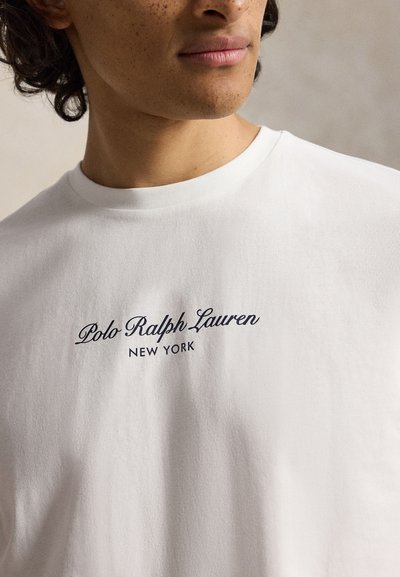Άτομο που φοράει λευκό t-shirt με το κείμενο "Polo Ralph Lauren New York" τυπωμένο στο στήθος.