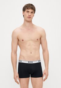 Μαύρα ανδρικά μπόξερ με λευκή ζώνη μέσης που φέρει το λογότυπο "BOSS", κατασκευασμένα από απαλό ύφασμα, εμφανιζόμενα σε μοντέλο χωρίς πουκάμισο.