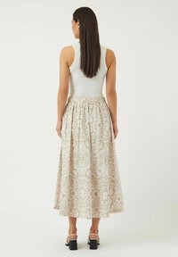 Maxi-skjørt med et blomstermønster i beige, elastisk midje og glatt tekstur. Kombinert med en tettsittende grå tank-top og sandaler med blokkheel.