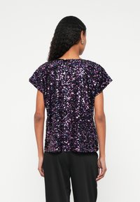 Top i lilla og sort med palietter, løs pasform, korte ærmer og rund halsudskæring. Glat tekstur med reflekterende palietter, der dækker stoffet.