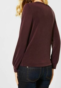 Długorękawowa bluzka w ciemnoczerwonym kolorze z gładkiej tkaniny. Dopasowany krój z delikatnym marszczeniem na ramionach i mankietach.