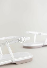 Weiße flache Sandalen mit dünnen, transparenten Riemen in strukturiertem Finish, einer quadratischen metallischen Schnalle und einer glatten, glänzenden Sohle.