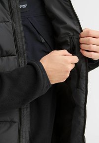 Crna puffer jakna s unutarnjim fleeced podstavljanjem. Ima zippered džep i vidljive šavove. Glatka tekstura i izdržljive patentne zatvarače.