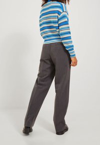 Gestreifter Pullover in Blau und Weiß, kombiniert mit grauen, gestreiften Hosen. Die Hosen haben ein gerades Bein und eine subtile Textur.