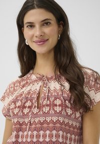 Rosa und creamfarbener BlUSE mit kurzen Ärmeln, Schlüssel-Ausschnitt und weichem Stoff mit floralem und geometrischem Muster.