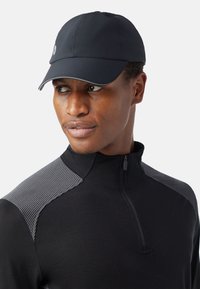 Gorra negra con visera curva, hecha de un material suave. El diseño presenta un logo sencillo y se combina con una parte superior negra con acentos grises texturizados.