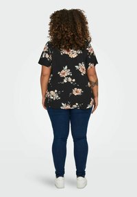 Blusa nera a fiori con maniche corte, caratterizzata da fiori rosa e bianchi. Abbinata a jeans blu e sneaker bianche, vista da dietro.