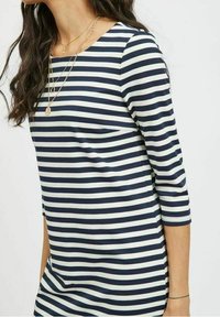 Námořnický a bílý pruhovaný top s třetinovými rukávy, kulatým výstřihem, jemnou texturou a volným střihem. Více jemných zlatých náhrdelníků.