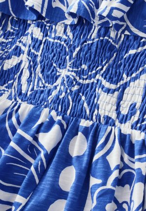 Blå og hvid blomstermønstret stof med smockedetaljer. Blød tekstur med samlet talje, designet til en løs, flydende pasform.