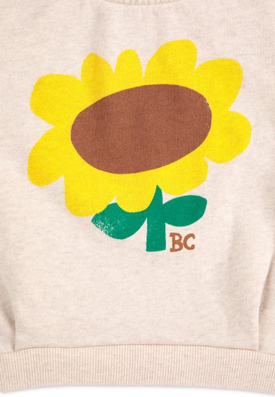Light beige fabric with a large yellow sunflower graphic, featuring a brown center and green leaves. Includes a small "BC" text detail.