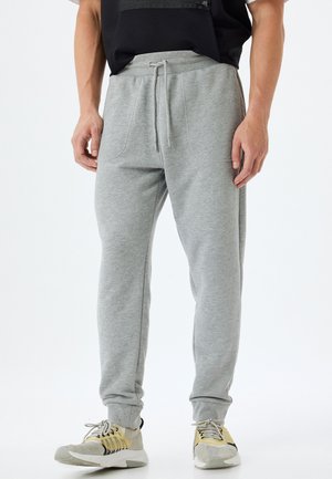 Pantalones de chándal grises hechos de una tela suave, con cintura ajustable, piernas ajustadas y bolsillos laterales. Combinados con zapatillas deportivas de color claro.
