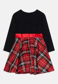 Zwarte lange mouw jurk met een rode satijnen tailleband en een rok in een rood, zwart en wit geruite stof, gezien vanaf de achterkant met ritsluiting.