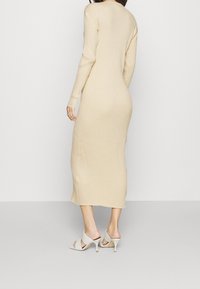 Lång beige ribbad klänning med långa ärmar, åtsittande silhuett och knälång nederkant. Kombineras med vita klackskor.