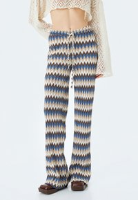 Gehaakte broek met een zigzagpatroon in beige, bruin en blauw. Heeft een elastische taille met trekkoord en een uitlopende silhouette.