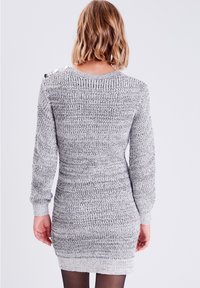 Robe pull grise en tricot avec manches longues, poignets côtelés et motif texturé. Comporte des boutons décoratifs sur l'épaule.