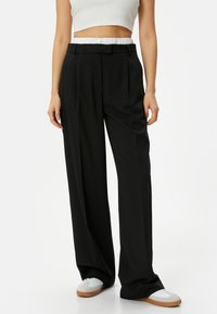 Zwarte wijde broek met een getailleerde pasvorm, voorzien van een knoopsluiting en een gestructureerde tailleband. Gecombineerd met witte sneakers.