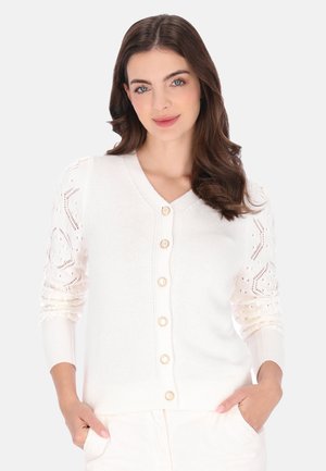 Hvid cardigan med V-hals, fem gyldne knapper og ærmer i struktureret strik med dekorativt mønster. Blødt materiale og figursyet design.