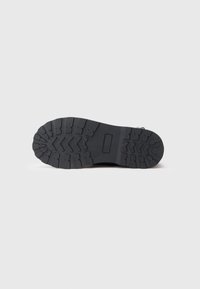 Sole in gomma nera con un dettagliato modello di trazione caratterizzato da solchi e creste per migliorare aderenza e stabilità. Design piatto e robusto.