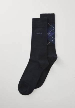 Calcetines de color marino; uno de color sólido con logo, otro con un patrón de argyle en tonos de azul con acentos blancos. Textura suave, mezcla de algodón.