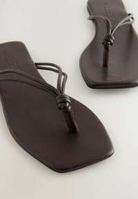 Sandales plates marron avec un dessus en cuir lisse, dotées de fines sangles et d'un accent noué sur le support de l'orteil. Design minimaliste de la semelle rectangulaire.