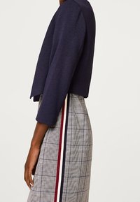 Giacca corta blu navy con maniche a tre quarti abbinata a un vestito a quadri con strisce rosse, bianche e blu navy lungo i lati.