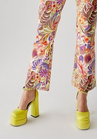 Pantaloni larghi con motivo floreale dai colori e dalle trame vivaci, abbinati a scarpe con tacco a blocco di un brillante colore giallo.