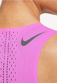 Gros plan sur l'épaule d'une personne portant un haut de sport sans manches rose vif avec des perforations noires et un logo Nike noir.