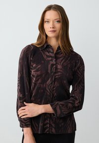 Blusa nera e bordeaux con righe verticali e motivo astratto, dotata di chiusura a bottoni sul davanti e maniche lunghe.
