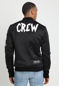 Giubbotto bomber in satin nero con "CREW" in grandi lettere bianche sul retro, colletto e polsini a coste, e etichetta "SIXTH JUNE" sull'orlo.