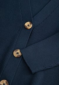 Granatowy kardigan, materiał prążkowany, dekolt w serek, trzy duże okrągłe guziki o naturalnym wykończeniu oraz prążkowane mankiety.