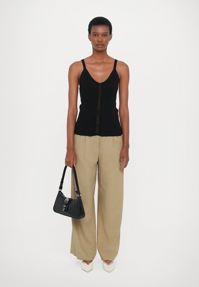 Schwarzes geripptes Tanktop mit V-Ausschnitt, cremefarbene weit geschnittene Hose, schwarze Handtasche mit silbernen Akzenten und weiße spitz zulaufende Absätze.