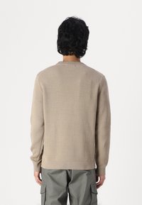 Beige knit sweater with a ribbed crew neck, long sleeves, and side slits, paired with olive green cargo pants.