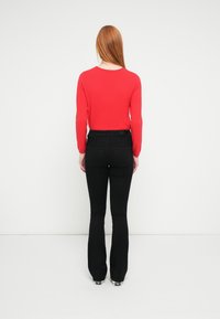 Czerwona bluzka z długim rękawem w połączeniu z czarnymi rozszerzanymi dżinsami, widziana od tyłu. Dżinsy mają gładkie wykończenie i dwie tylne kieszenie.