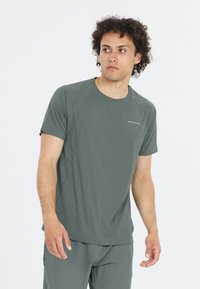 Tumma vihreä urheilupaita, jossa on lyhyet hihat, pyöreä pääntie ja teksturoitu kangas. Ominaisuuksiin kuuluu vaalea ommel ja pieni logo rinnassa.