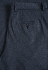 Tummansinisiä, teksturoituja kangashousuja, joissa on takatasku mustalla napilla. Hoikka vyötärö ja räätälöity muotoilu näkyvät.