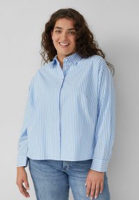 Lichtblauw en wit gestreept overhemd met een spread collar en lange mouwen. Heeft een losse pasvorm en een afgeronde zoom.