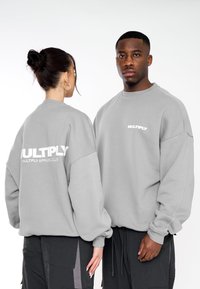 Felpe grigie oversize con logo bianco "MULTIPLY" sul davanti e dietro, spalle scese e polsini a costine.