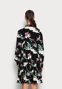 Vestido preto com padrões florais e de pássaros. Apresenta mangas longas, gola e um design de saia em camadas. O tecido parece texturizado.