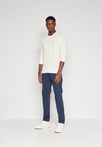 Knit cream sweater with ribbed cuffs, paired with navy trousers. White sneakers complete the outfit. Simple design and color palette.