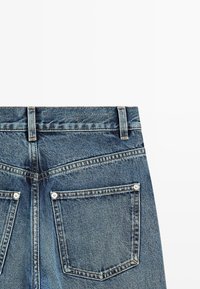 Jeans in denim con una lavatura blu media, caratterizzati da vita alta, due tasche posteriori con rivetti in metallo e dettagli cuciti lungo le cuciture.