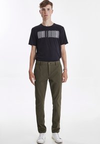 Sort T-shirt med hvidt grafisk design, olivengrønne bukser og hvide sneakers. Bukserne har knaplukning og sidelommer.
