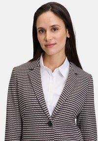 Blazer pied-de-poule noir et blanc avec un bouton unique, coupe ajustée, revers crantés, associé à une chemise blanche à boutons.