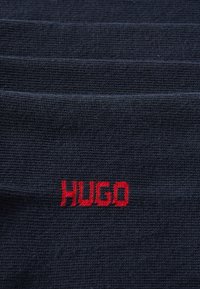 Marine tekstil med ribbet struktur, der har et rødt broderet "HUGO"-logo placeret centralt.