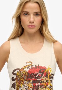 Débardeur crème avec un col rond, orné d'un graphique de tigre embelli et du texte 'REAL' en cristaux colorés.